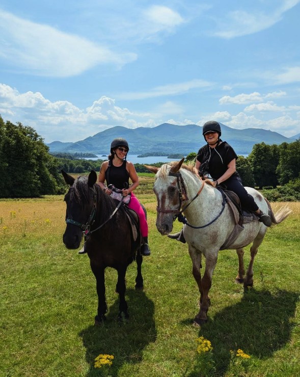 Two riders on horseback in a meadow above the Lakes of Killarney, mountains on the skyline