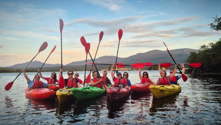 Kayakers raising their paddles together on the Lakes of Killarney with the mountains beyond